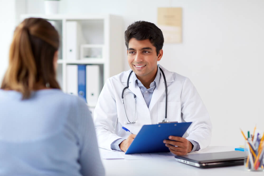 Smiling Doctor With Clipboard and Patient at Hospital