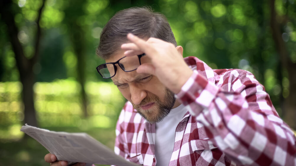 Male Trying to Read Newspaper in Park With Poor Sight